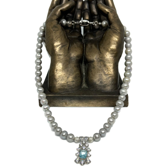 8-9mm AAA Quality Freshwater Pearl Necklace in Silver with Aquamarine Party Drop viewed from the front and hanging from a brass sculpted pair of hands.