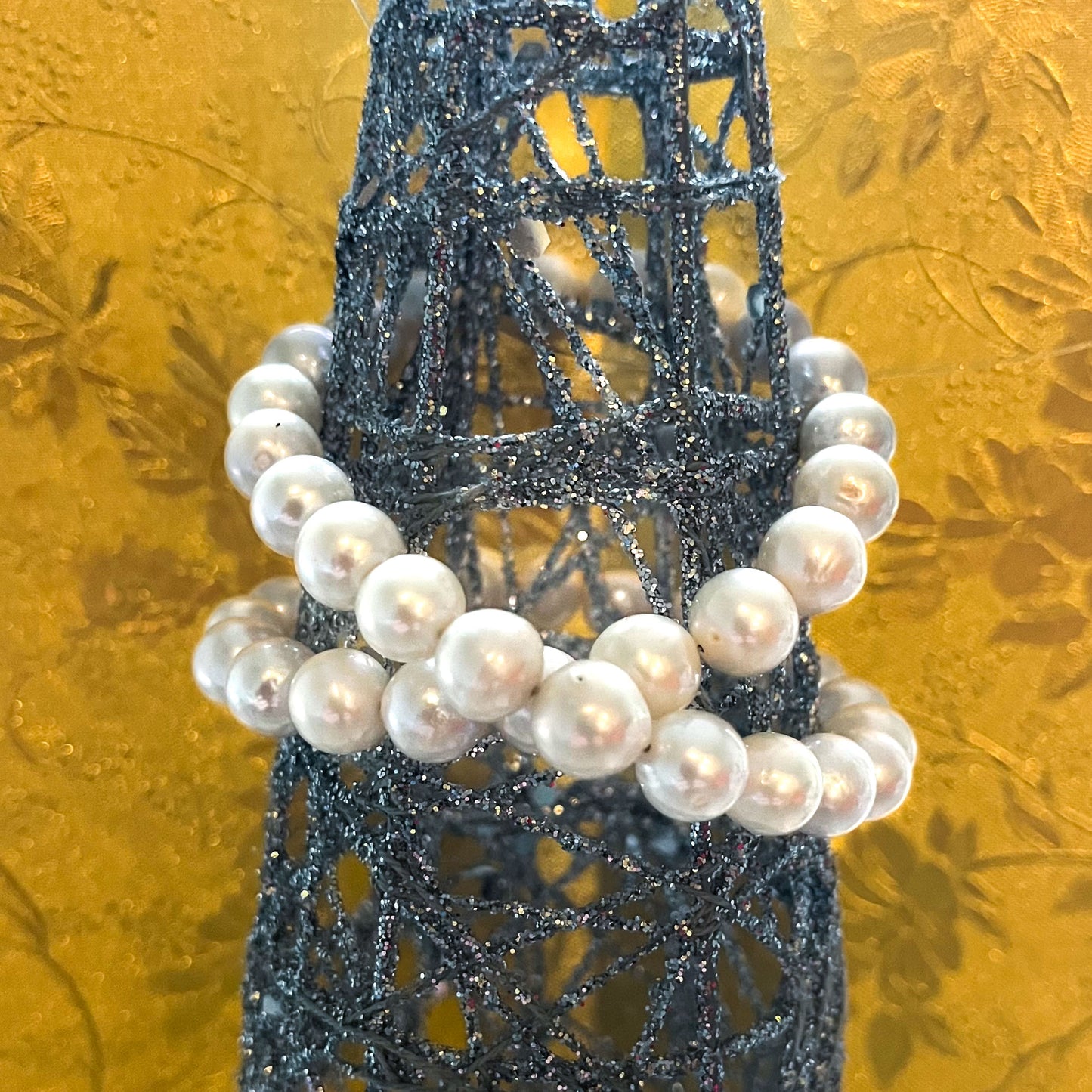 Photo of 10mm AAA Quality Freshwater Cultured Pearl Necklace in White hung from an ornament and a gold floral pattern background.